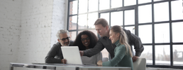 A group of four people looking at a laptop on a table