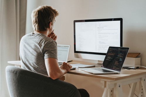 A person with short hair and a grey tshirt sitting at a desk in front of a computer