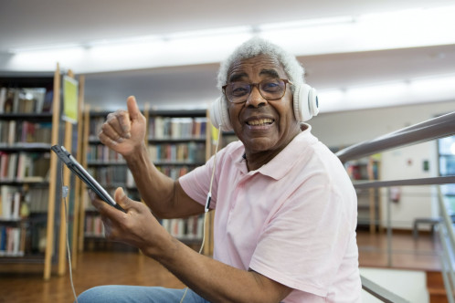 A smiling man wearing headphones reading a book on an e-reader
