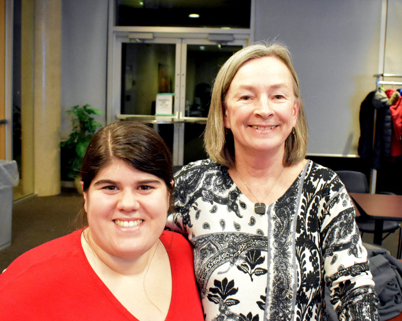 Two smiling women, one with brown hair and a red shirt and another with blonde hair and a black and white shirt