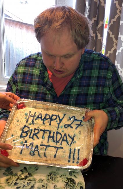 Matthew holds a cake that says Happy 27 Birthday Matt