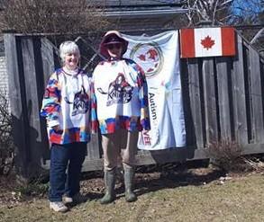 Two women stand in their backyward in front of the World Autism Day flag hanging from their fence