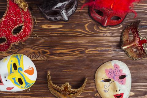seven theatre masks laid out in a circle on a brown wooden table