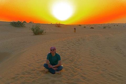 Paul Walderman sitting cross-legged in a desert with a gorgeous sunrise in the background.