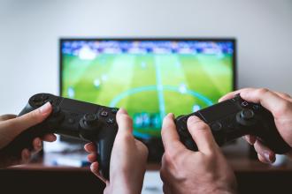 two sets of hands on playstation controllers playing a soccer game