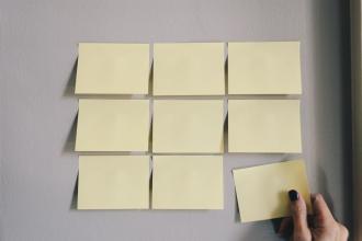 9 yellow sticky notes on a wall with a person's hand grabbing one in the bottom right corner