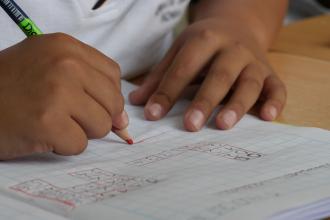 Child writing in a graphing notebook at a desk